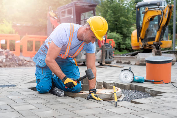 Concrete contractor in Albany, CA laying interlocking paving stones around a sewer manhole as part of a patio installation project.